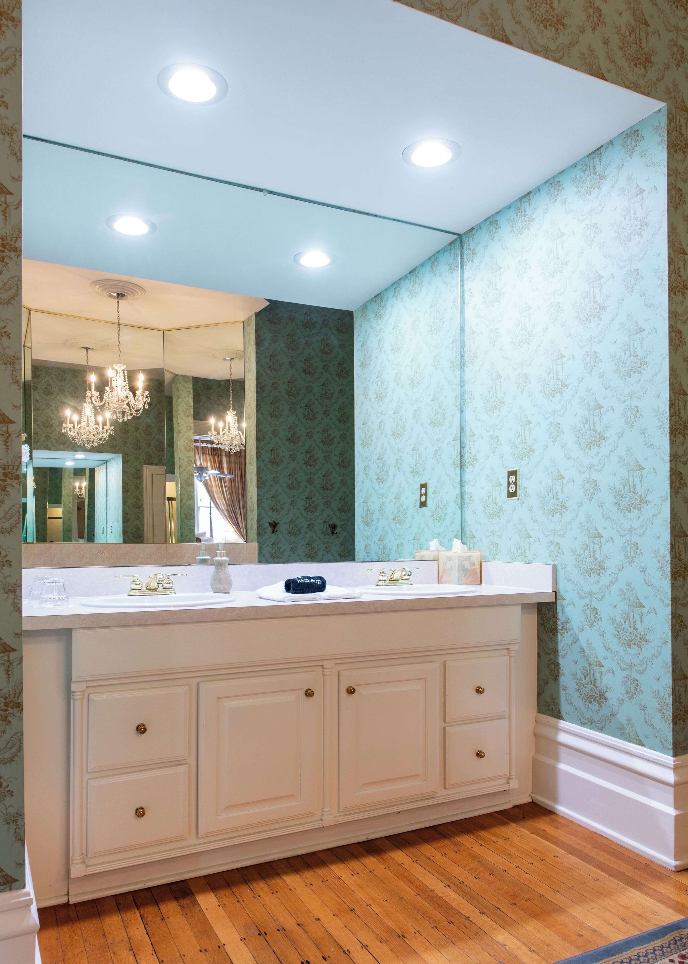 A bathroom with a large mirror, vanity, and a chandelier.