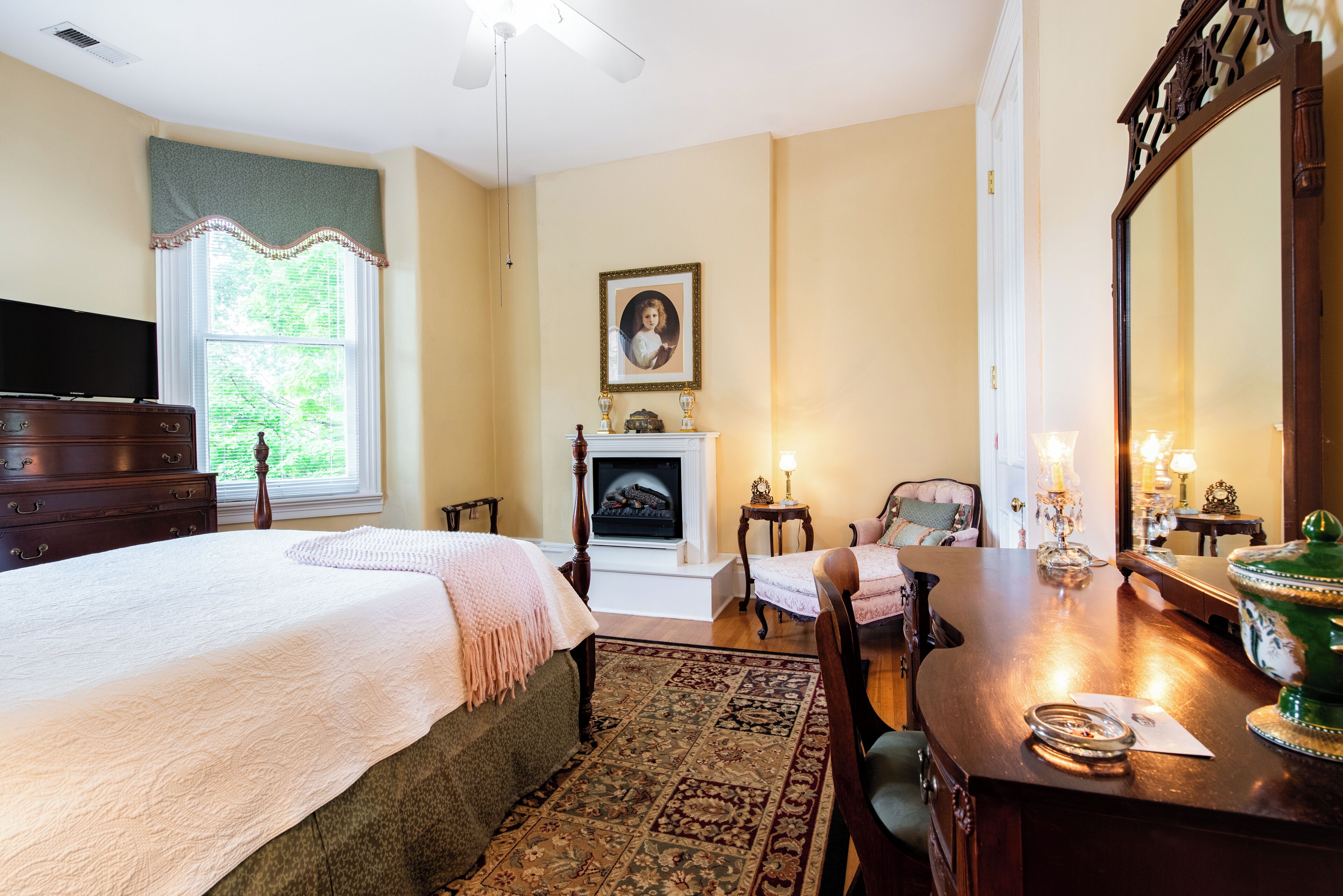 Une chambre à coucher comprenant un lit, une commode, une chaise, une cheminée et un grand miroir.