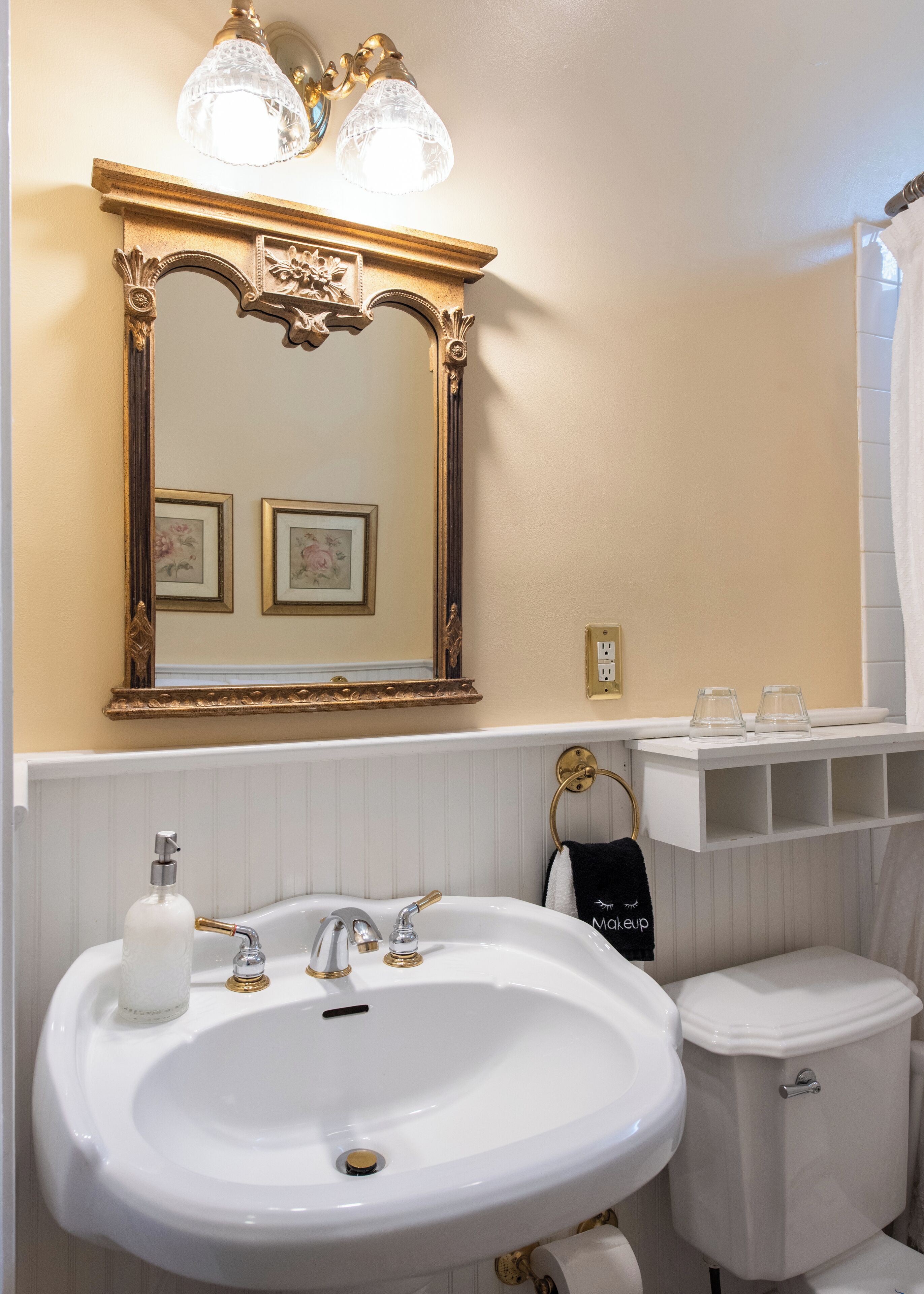 A bathroom with a white sink, gold faucets, a gold-framed mirror, and a toilet.