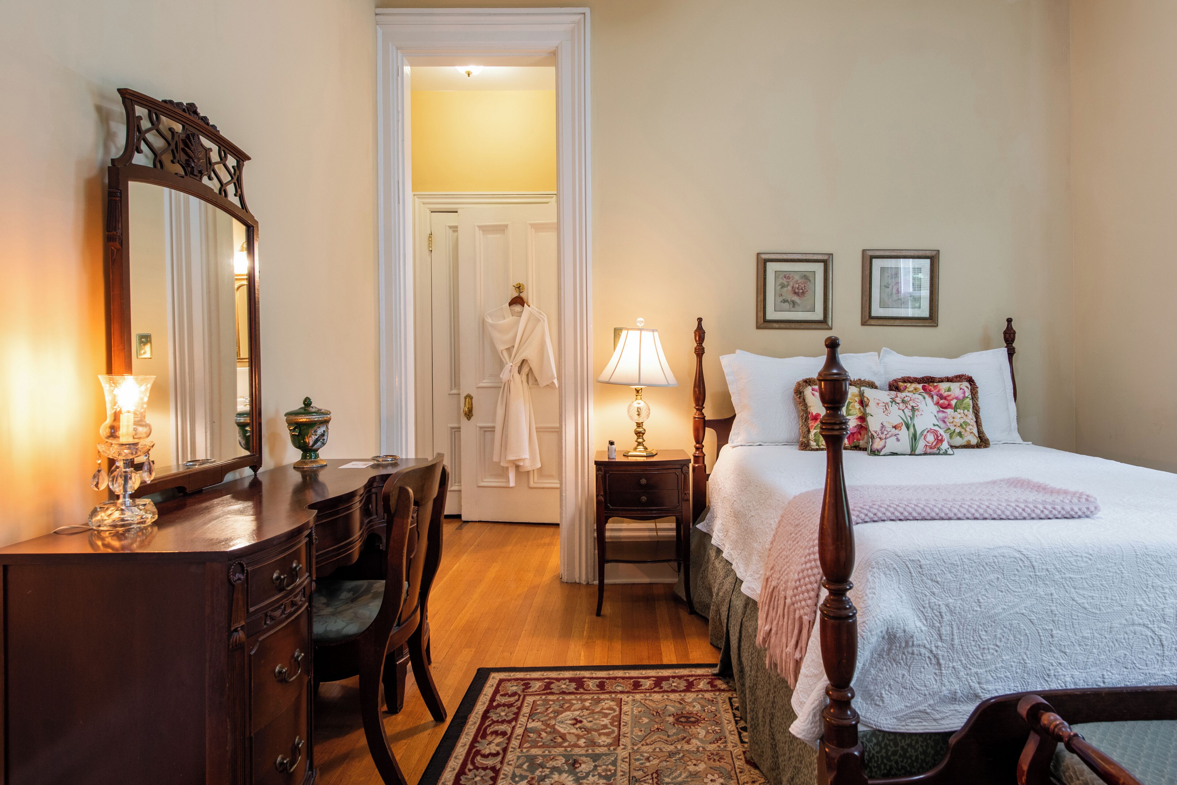 Un dormitorio con cama con dosel, cómoda de madera, espejo y mesita de noche con lámpara.