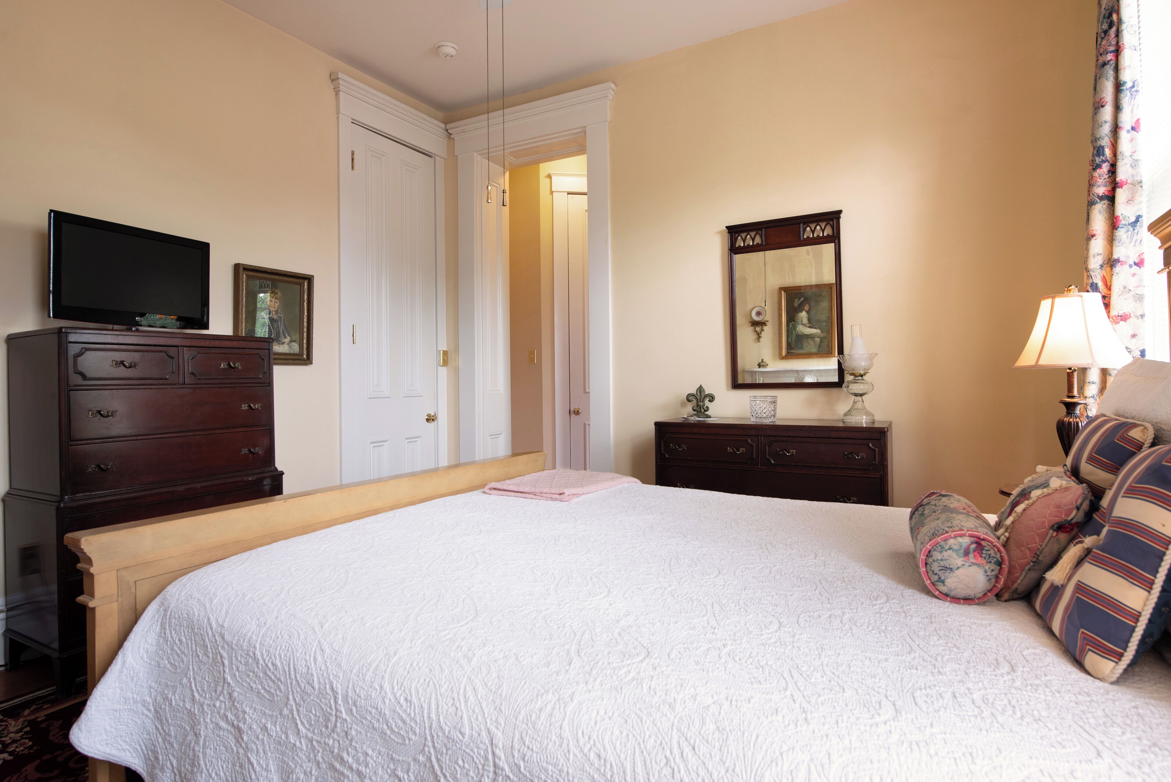 Een hotelkamer met een groot bed, een dressoir, een televisie, een spiegel en een lamp.