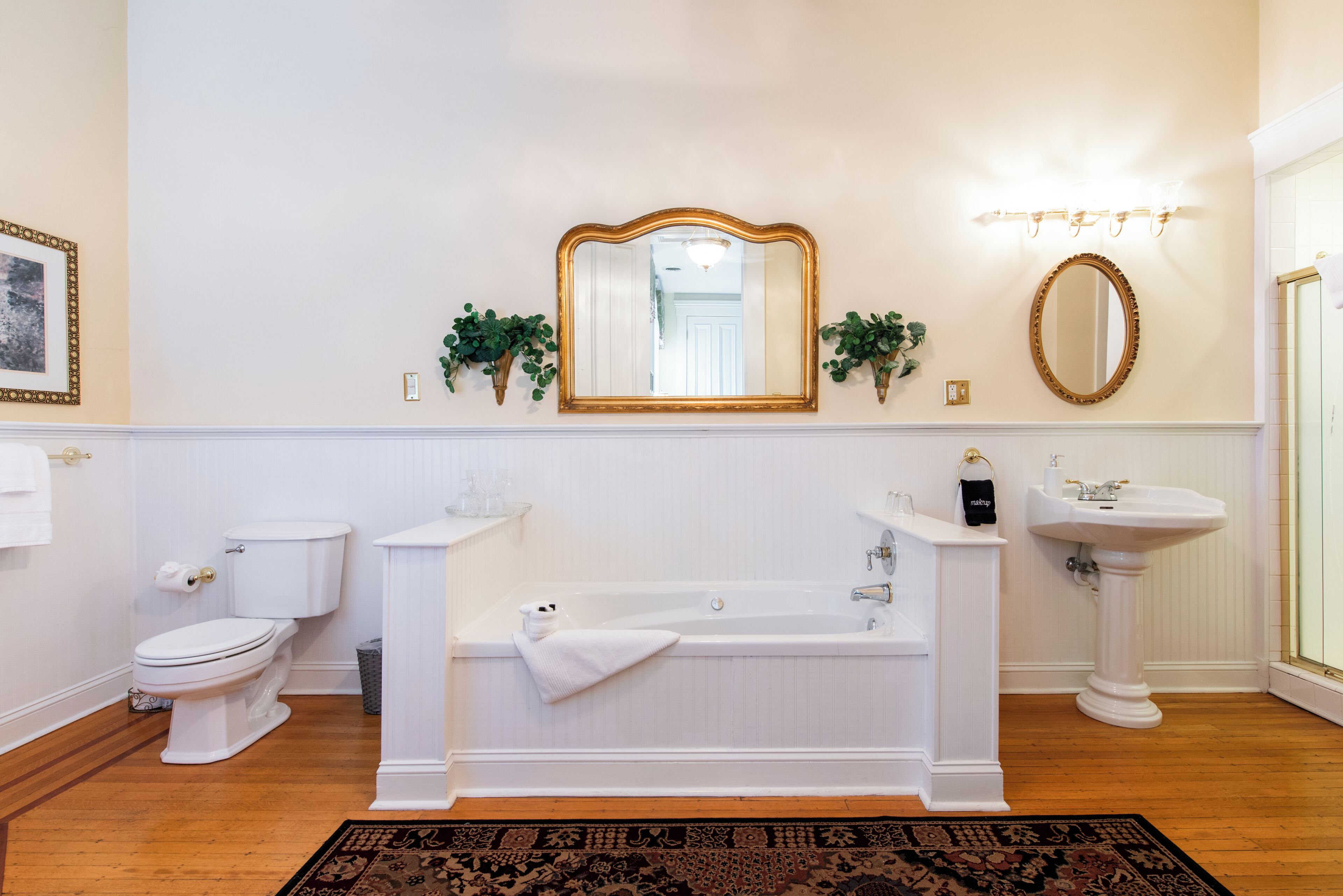 Une salle de bain avec une baignoire blanche, un lavabo sur colonne, des toilettes et deux miroirs fixés au mur.