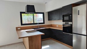 A modern kitchen with a wooden island, black cabinets, a stainless steel refrigerator, and a window with a view of greenery. - VILLA REVA with swimming pool, between land and sea (Nézignan-l'Évêque)
