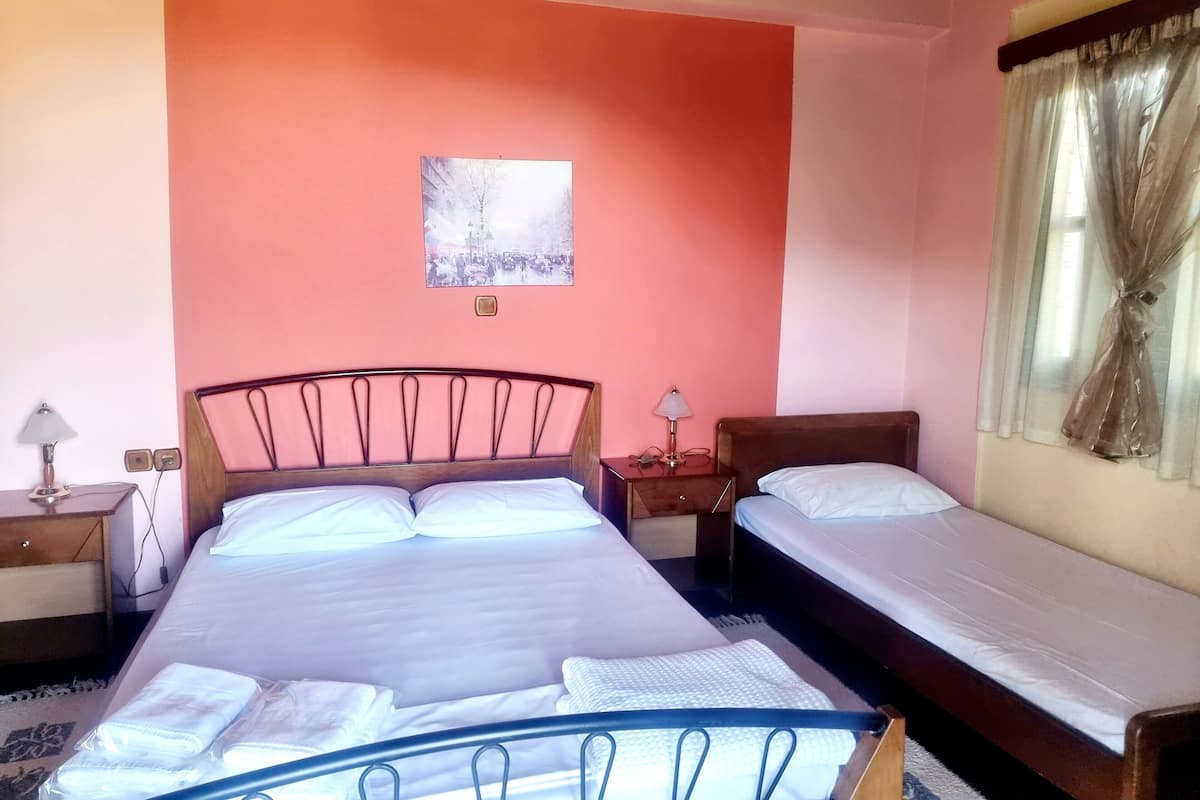 Une chambre à coucher avec un grand lit, un plus petit lit, une table de chevet, une lampe et une fenêtre avec des rideaux.