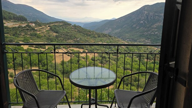 Een balkon met twee stoelen en een tafel, met uitzicht op een bergachtig landschap.