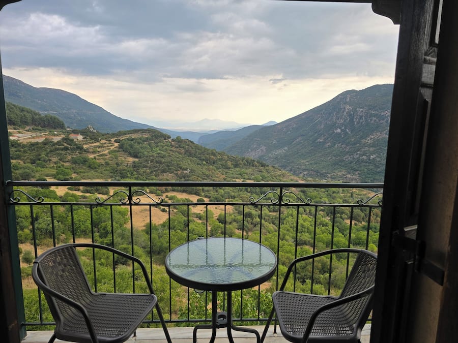 A balcony with two chairs and a table, overlooking a mountainous landscape.