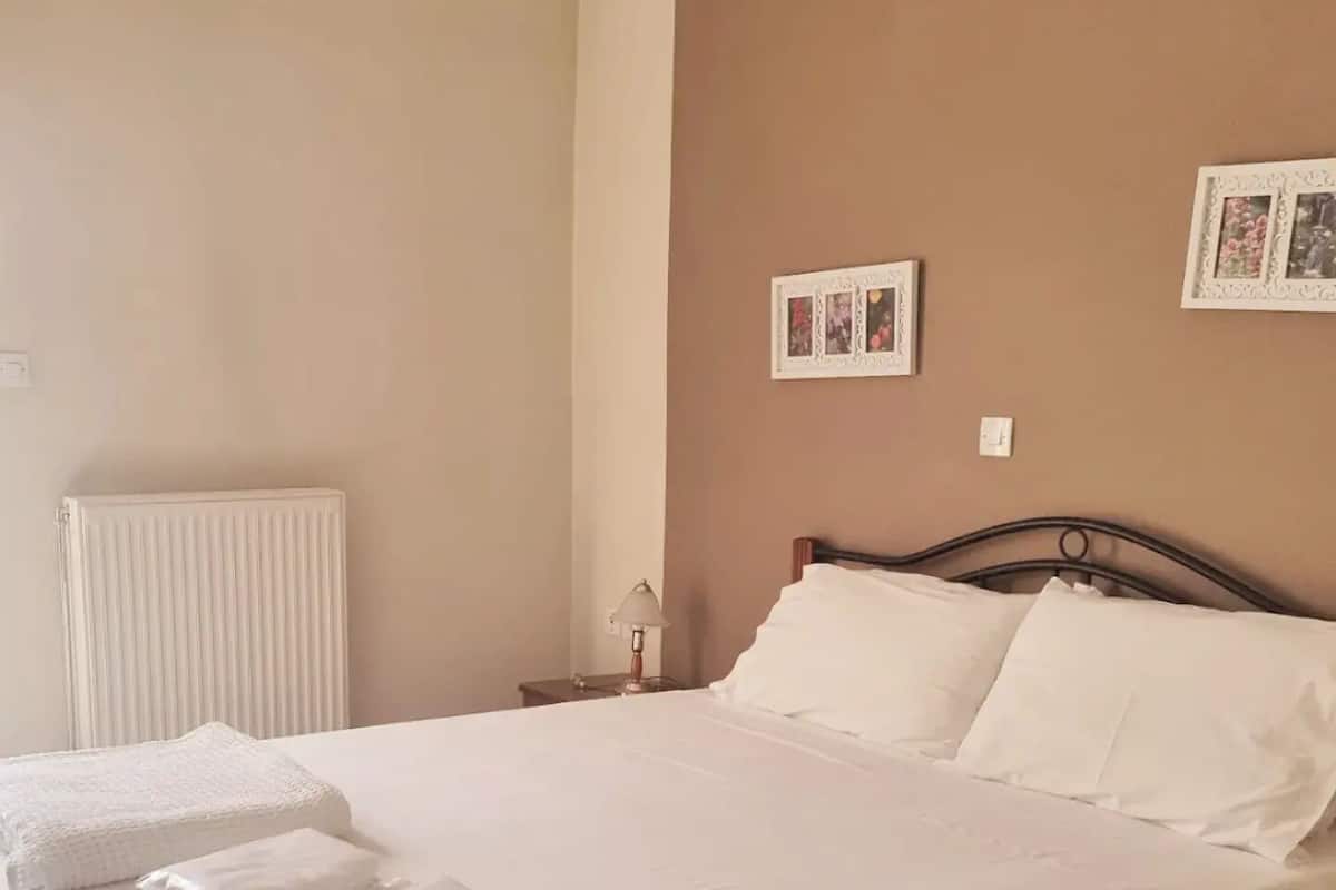 Un lit bien fait, avec du linge de lit blanc et des oreillers, une table de chevet avec une lampe et un radiateur au mur.