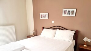 Een net opgemaakt bed met witte lakens en handdoeken, een houten hoofdbord, twee nachtkastjes met lampen, en twee ingelijste foto's aan de muur.