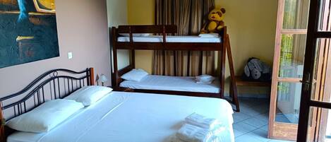 A room with bunk beds, a large bed, a painting on the wall, and a window with curtains.