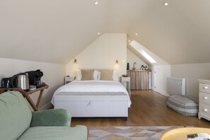 A bedroom with a bed, bedside tables, a coffee maker, a radiator, and a view of the kitchen.