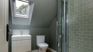 A bathroom with a white toilet, a sink, and a shower area with glass doors. - Cosy one bedroom apartment - Keepers Annexe (Cranham)