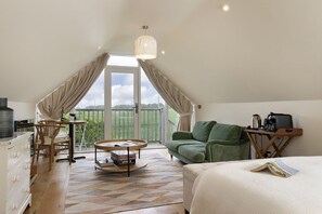 Een gezellige loft slaapkamer met een groot raam, een groene bank, een houten tafel en een bed met een tijdschrift erop.