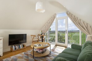 Un salon confortable avec un téléviseur, des livres, une table basse ronde et un canapé vert.