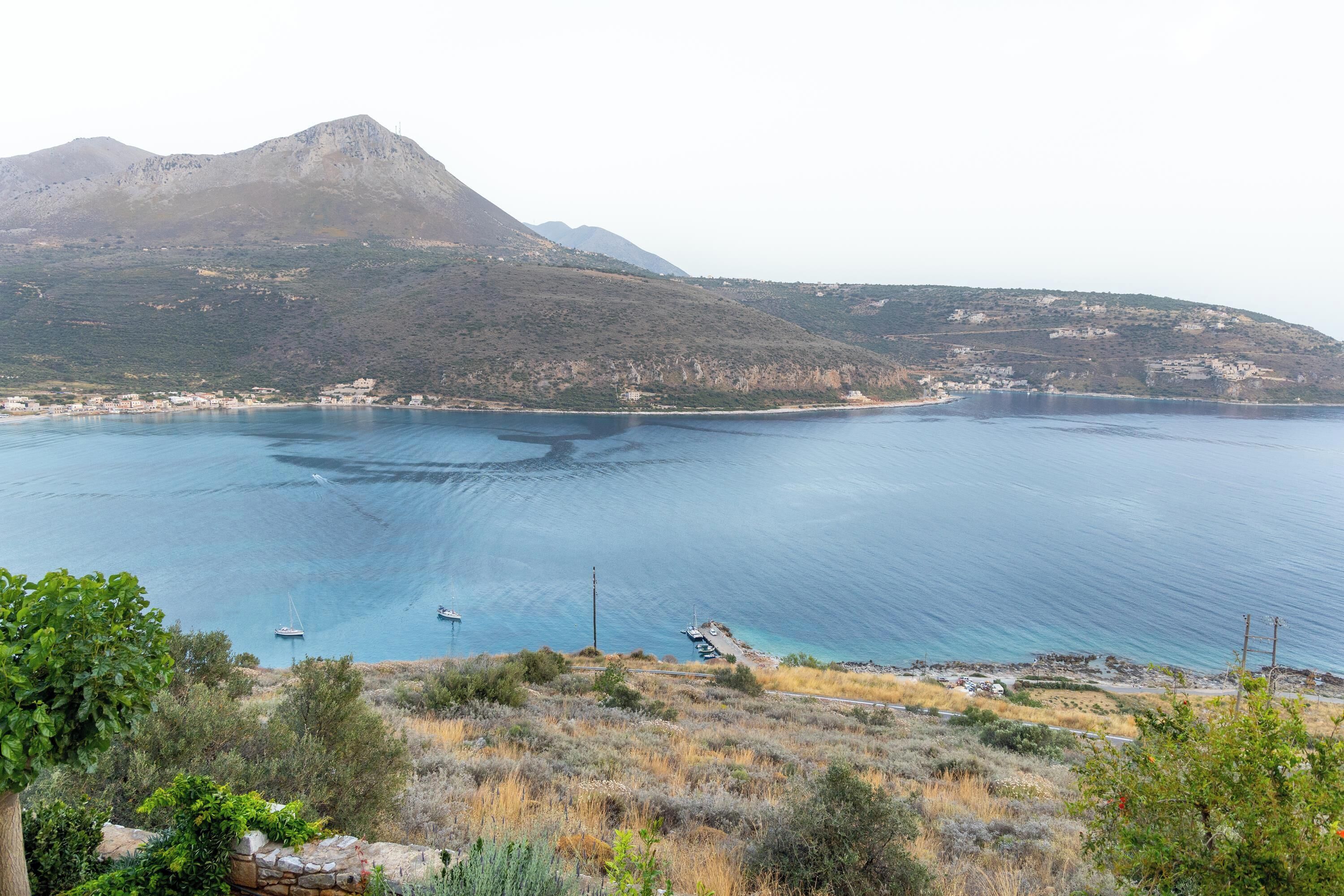A coastal landscape with a mountain, clear blue sea, and sparse vegetation.