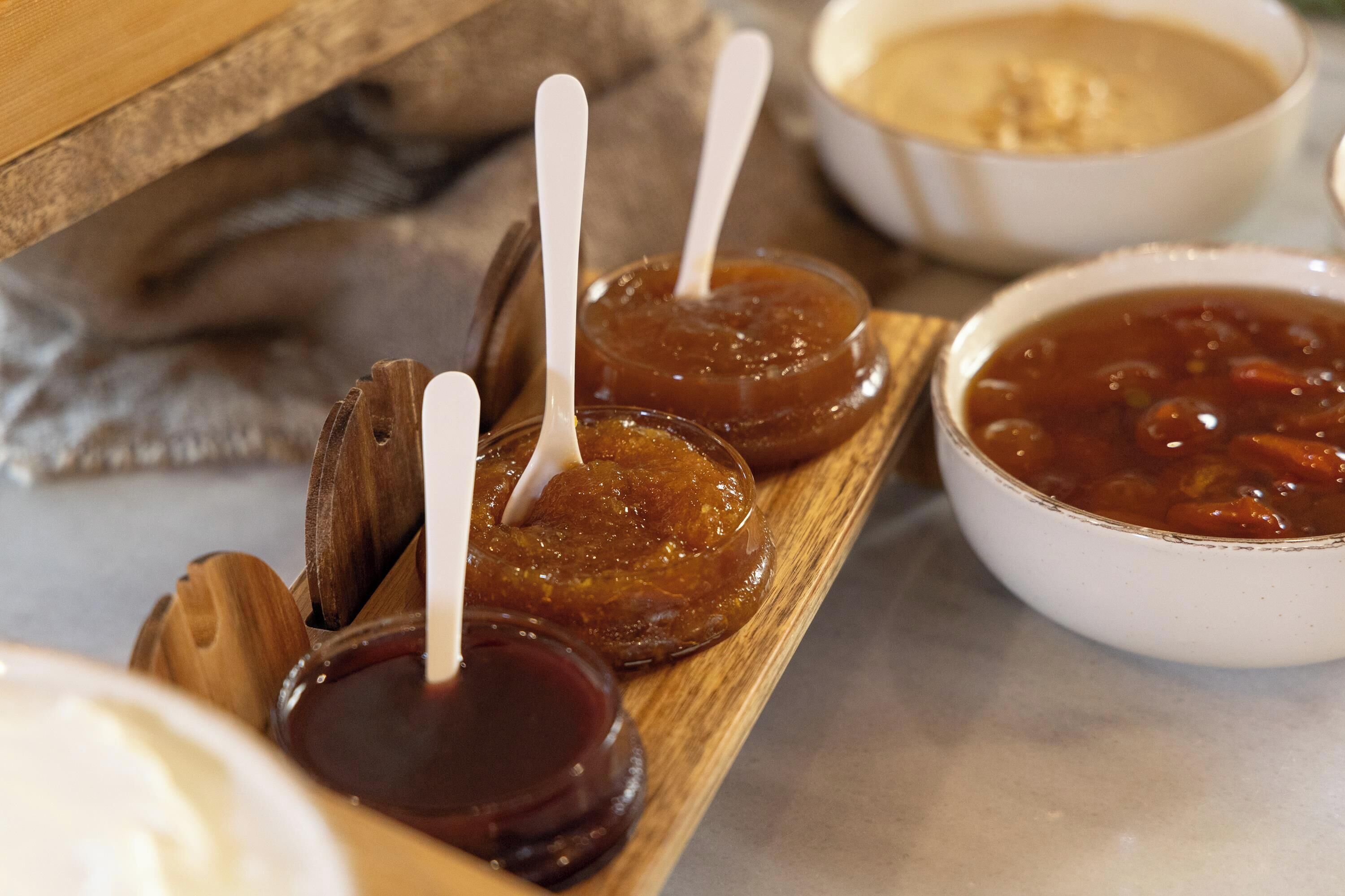 A wooden tray with jars of preserves and a bowl of soup.