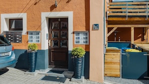 Un edificio con fachada marrón texturizada, una puerta de madera con paneles de vidrio y dos macetas grandes con plantas.