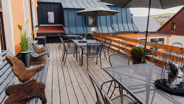 Una terraza en la azotea con mobiliario exterior, una mesa y un gran paraguas.