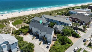 A coastal residential area with a large house featuring a balcony, surrounded by lush greenery and a beach in the background. - Ocean Views, Beach Access, Luxury Townhouse - Sleeps 10, Ping Pong! (Wrightsville Beach)