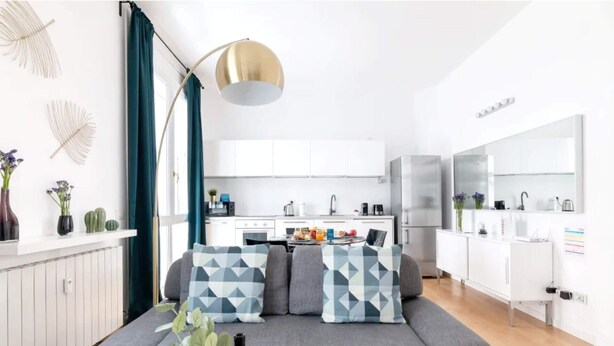 A modern living room with a grey sofa, a coffee table with drinks, and a kitchen in the background.
