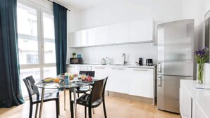 A modern kitchen with white cabinets, a stainless steel refrigerator, and a dining table with chairs.
