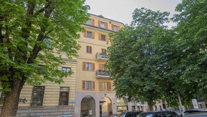 Un immeuble à plusieurs étages avec une façade jaune, des voitures garées et des arbres au premier plan.