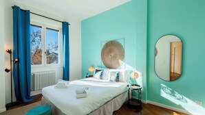 A bedroom with a bed, a round mirror, a bedside table, a window with curtains, and a radiator. - Sweett | Mentana IV - Two Bedroom Apartment, Sleeps 3 (Milano)
