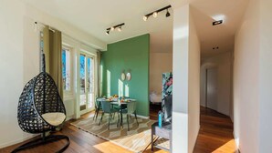 A modern living room with a dining area, a green accent wall, and a black hanging chair. - Sweett | Mentana IV - Two Bedroom Apartment, Sleeps 3 (Milano)