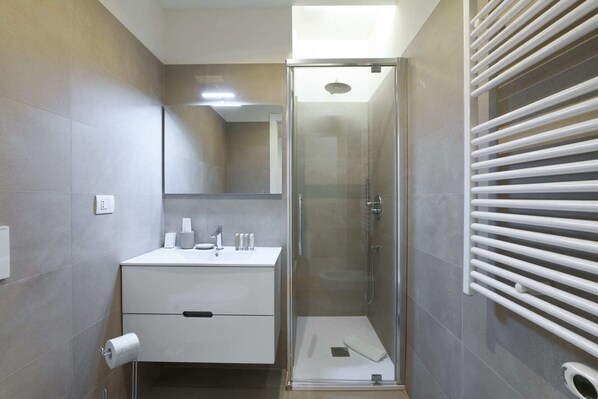 Une salle de bain moderne avec une douche à parois de verre, un lavabo blanc avec des articles de toilette et un porte-serviettes.