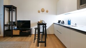 A compact kitchen with a black TV, a small dining table with stools, a microwave, and a coffee machine.