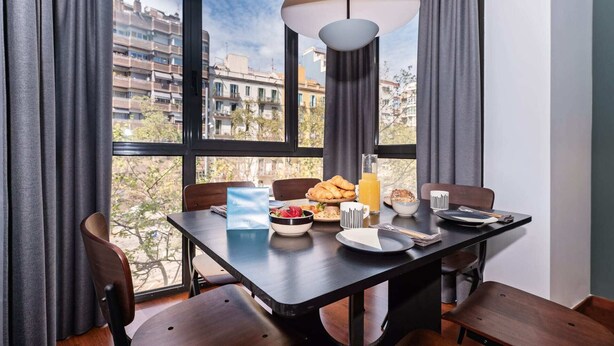 Ein Essbereich mit einem für das Frühstück gedeckten Tisch, mit Croissants, Obst und Saft, und Blick auf die Stadt durch große Fenster.