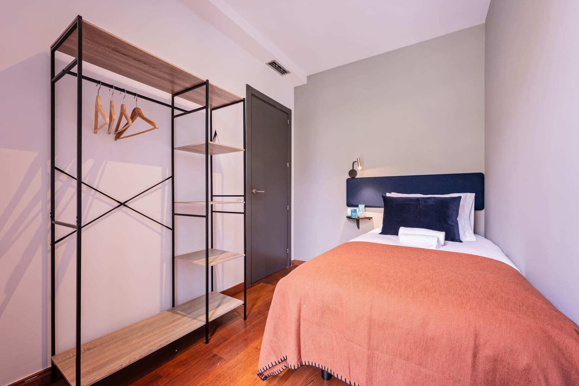 Een slaapkamer met een bed, nachtkastje, inbouwkast met planken en een deur.