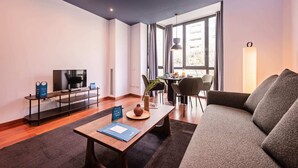A modern living room with a flat-screen TV, a dining area with a table and chairs, and a large window providing natural light. - Sweett | Roma 3B - One Bedroom Apartment, Sleeps 4 (Barcelona)