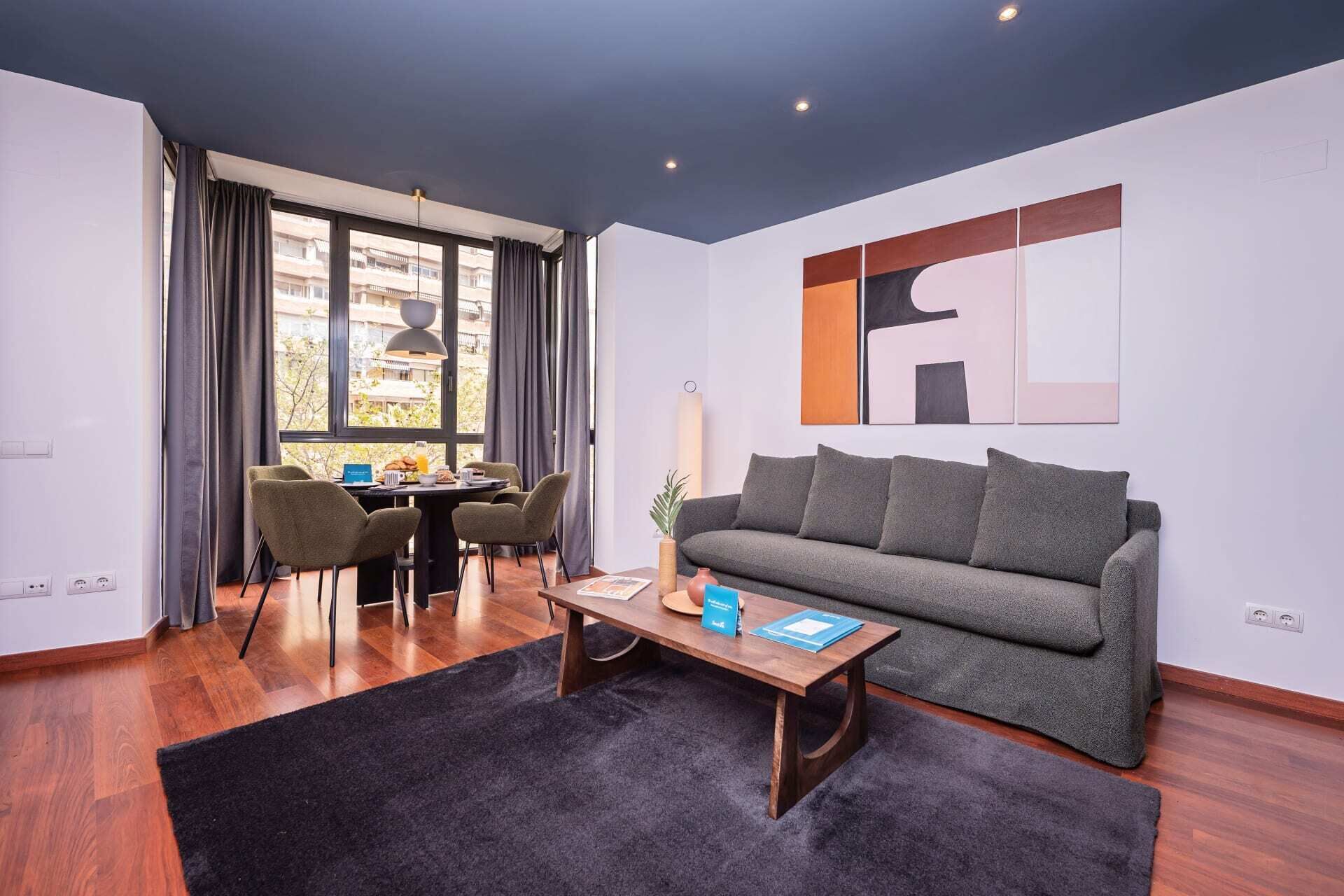 A modern living room with a grey sofa, a wooden coffee table, and a dining area with a table and chairs.