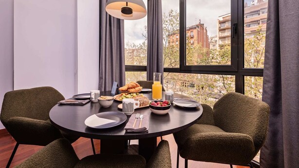 A dining area with a round table, two chairs, and a window with a view of buildings. - Sweett | Roma 3B - One Bedroom Apartment, Sleeps 4 (Barcelona)