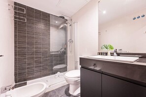 Ein modernes Badezimmer mit einer Duschkabine, einer weißen Toilette und einem schwarzen Waschtisch mit Spiegel.