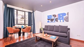 A modern living room with a grey sofa, orange chairs, a wooden coffee table, and abstract art on the wall. - Sweett | Roma 5B - One Bedroom Apartment, Sleeps 4 (Barcelona)