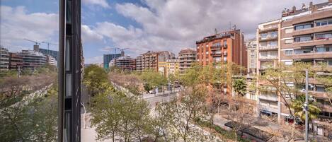 A cityscape with multi-story buildings, a construction site, and a street with trees and parked cars.