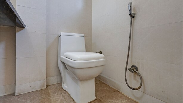 A bathroom with a toilet, a shower, and tiled walls. - Mauryan Elite Hotel Qutab Minar Metro Station (New Delhi)