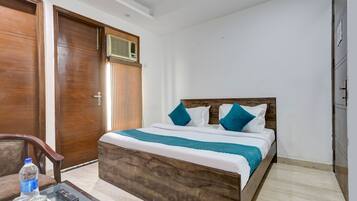 Habitación de hotel ordenada con una cama de madera, una mesita de vidrio con un control remoto y una botella de agua.