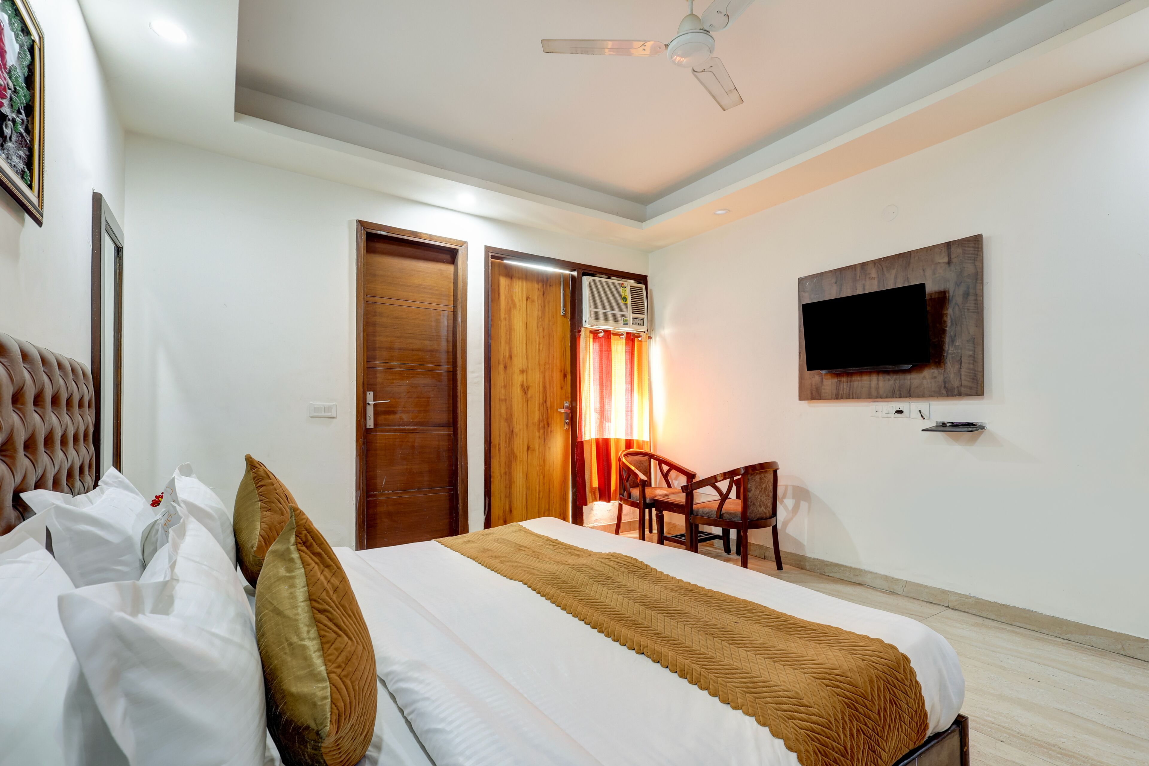 A hotel room with a bed, a chair, a television mounted on the wall, and a ceiling fan.