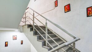 Un escalier avec des rampes en métal et des marches en granit, menant à un palier avec un mur blanc et de petits tableaux encadrés.
