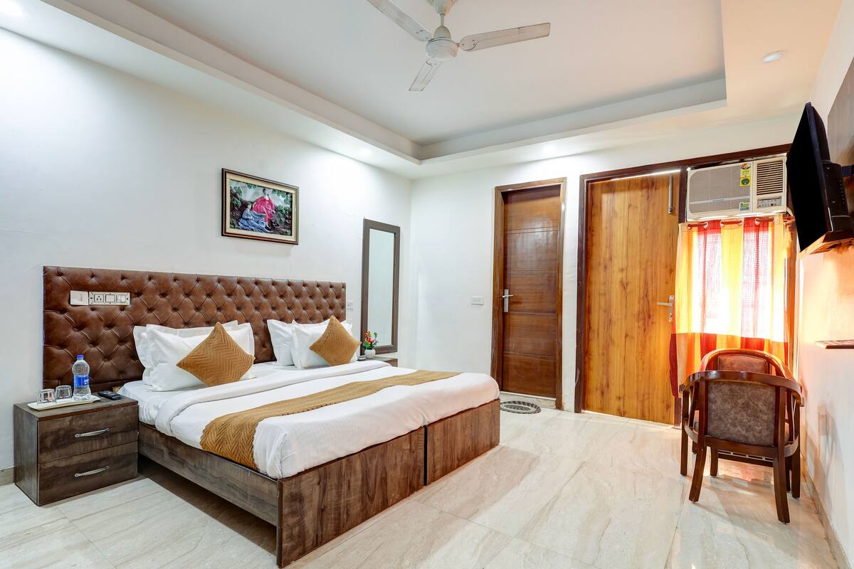A bedroom with a large bed, a nightstand, a chair, a ceiling fan, and a TV.