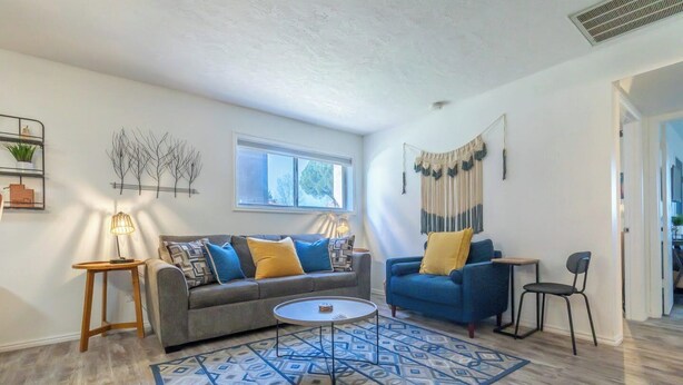 A living room with a grey sofa, blue armchair, and a patterned rug. - Charming 2-bedroom condo with pools, courts and more in St. George (St. George)