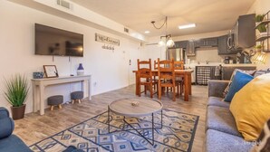 A modern living room with a sofa, coffee table, and dining area. There is a TV mounted on the wall, a kitchen in the background, and a welcome sign. - Charming 2-bedroom condo with pools, courts and more in St. George (St. George)