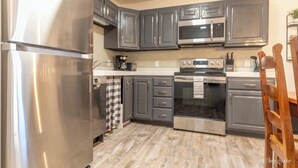 A modern kitchen with stainless steel appliances, dark grey cabinets, and a wooden floor. - Charming 2-bedroom condo with pools, courts and more in St. George (St. George)