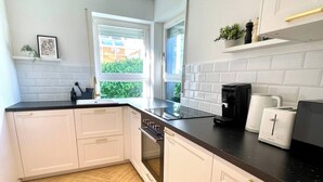 Cocina moderna con armarios blancos, encimera negra y ventana con vistas a la vegetación.