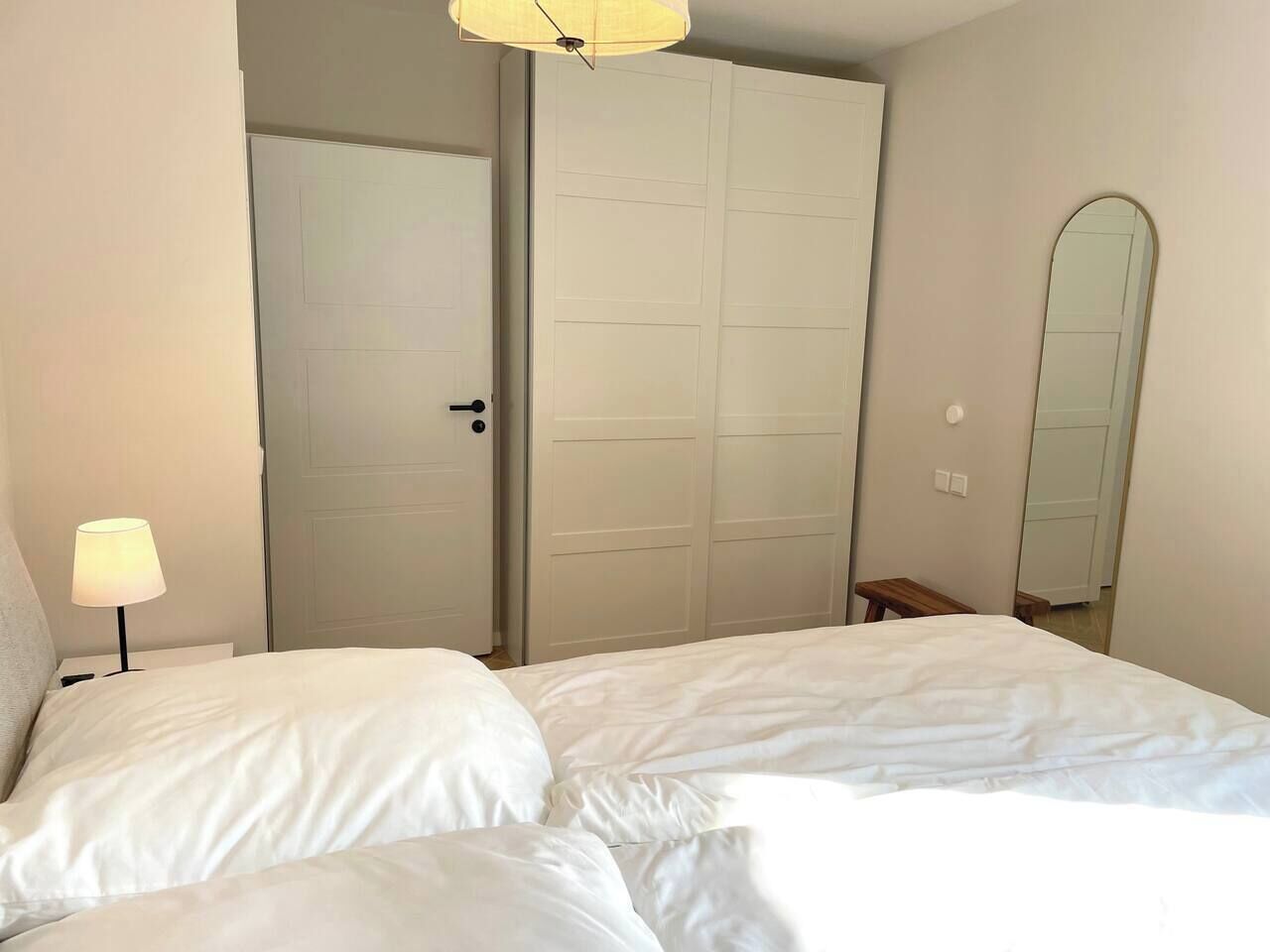 A bedroom with a bed, a nightstand, a lamp, a wardrobe, and a mirror.