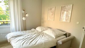 Una cama con una colcha blanca y almohadas, una mesita de noche y una lámpara.