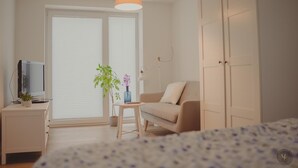 A bedroom with a bed, a TV on a nightstand, a sofa, a small table with a plant, and a wardrobe.