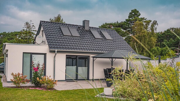 A modern house with a sloped roof, large windows, and a covered patio area.
